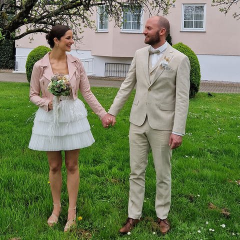 Paar im Garten zeigt Brautkleid und Anzug für die Hochzeit
