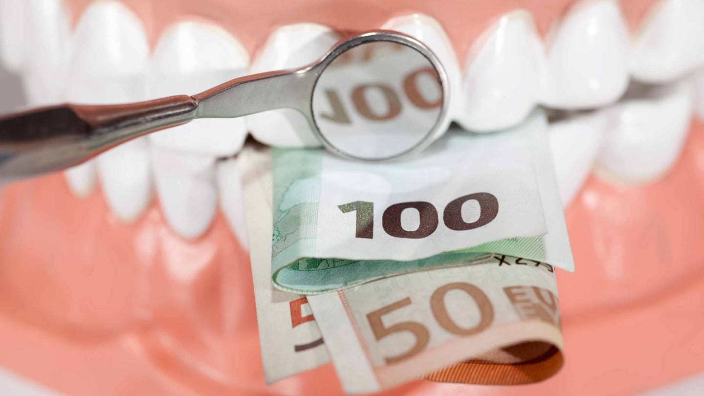 Vor einem Gebiss mis Zähnen liegen mehrere Euroscheine. In einem Zahnarztspiegel spiegelt sich die Zahl 100.