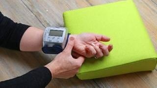 Arm liegt auf einem Kissen, mit einem Blutdruckmessgerät wird der Blutdruck am Handgelenk gemessen