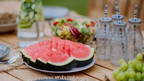 Gedeckter Tisch im Freien mit Melone, Salat, Wasserflaschen