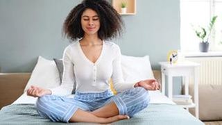 Frau sitzt in Yoga-Pose auf dem Bett