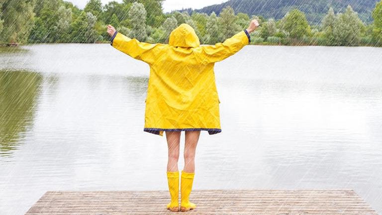 Frau steht am See und hat eine Regenjacke an