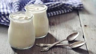 Zwei Glässer mit probiotischem Joghurt stehen auf einem Holztisch