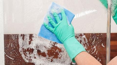 Eine Frau putzt die Scheibe einer Duschkabine - Kalk entfernen