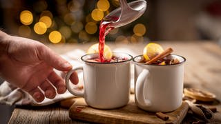 Glühwein wird mit einer Kelle in Tassen geschöpft