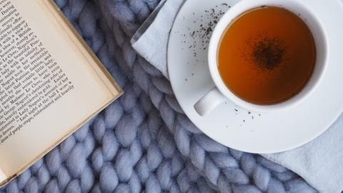 Teetasse und Buch auf einer Decke