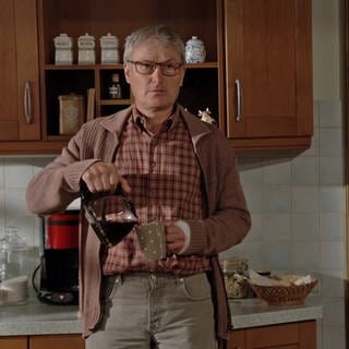 Karl steht in der Küche und gießt sich Kaffee in einen Becher