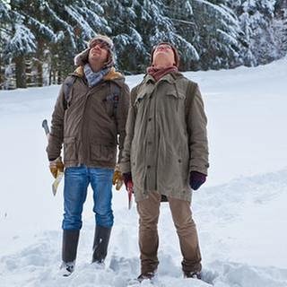 Andreas und Karl stehen im tiefen Schnee am Waldrand und schauen in den Himmel