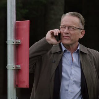 Bernhard Faller steht an einer Bushaltestelle und telefoniert