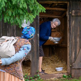 Johanna holt Eier aus dem Hühnerstall, Lioba steht mit ihrem Leiterwägele davor