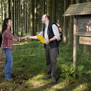 Bea und Monique begrüßen den Prüfer vor dem Schild zum Wonnepfad