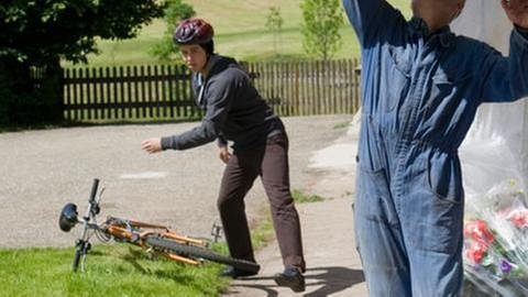 Karl repariert eine Dachrinne vor dem Fallerhof, Sebastian kommt dazu und legt gerade sein Fahrrad ab