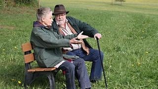 Hermann und Johanna sitzen auf einer Bank auf der grünen Wiese