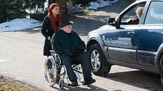 Jenny schiebt Hermann in seinem Rollstuhl, Bea sitzt in ihrem Wagen