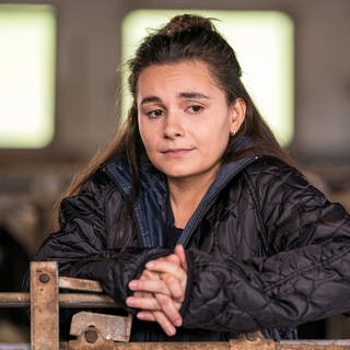 Jenny steht nachdenklich im Stall an ein Gatter gelehnt