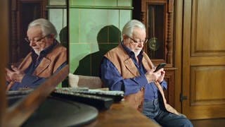Hermann sitzt am Kachelofen und daddelt mit dem Handy