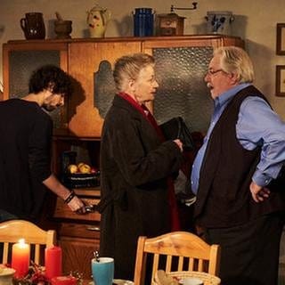 Johanna spricht mit Hermann, Albert sucht etwas im Küchenschrank