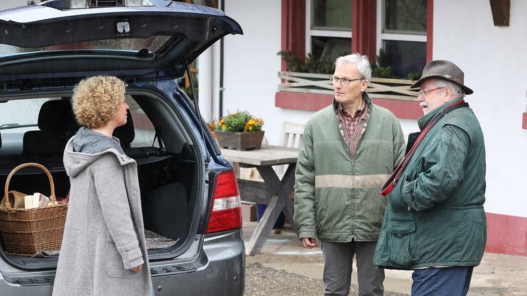 Bea, Karl und Hermann stehen vor dem geöffneten Kofferraum von Karls Wagen