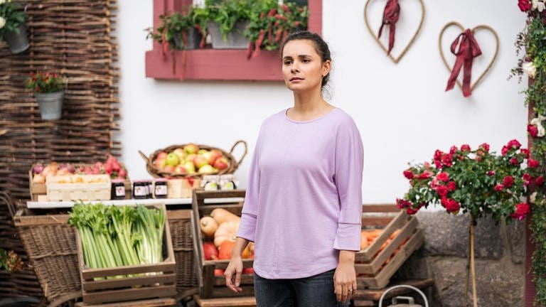 Jenny (Julia Obst) steht nachdenklich vor dem mit Gemüse bestückten Hofladen
