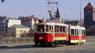 Historischer roter Zug in Prager Altstadt mit Lokführer und mehreren Menschen im Abteil