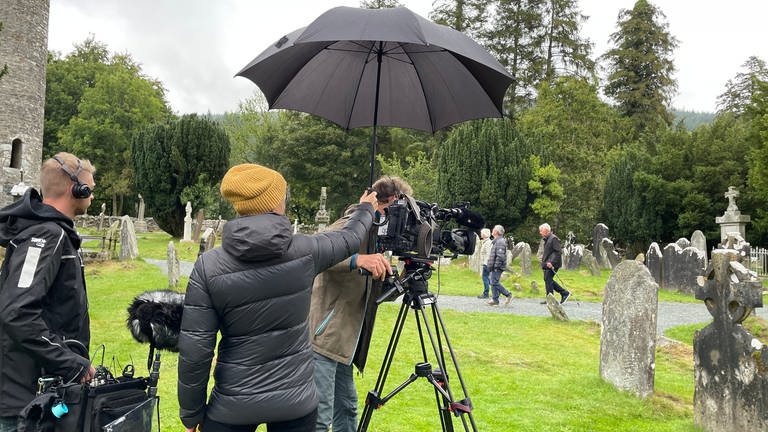 Der Regenschirm ist ein ständiger Begleiter auf der grünen Insel, auch bei den Dreharbeiten auf dem Friedhof von Glendalough.