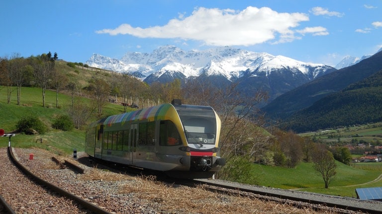 Die Strecke der Vinschgaubahn ist sechzig Kilometer lang, Wir fahren von Mals hinab ins das von der Sonne verwöhnte Meran. Im Hintergrund bedeckt im Frühjahr die Berge noch mit Schnee.