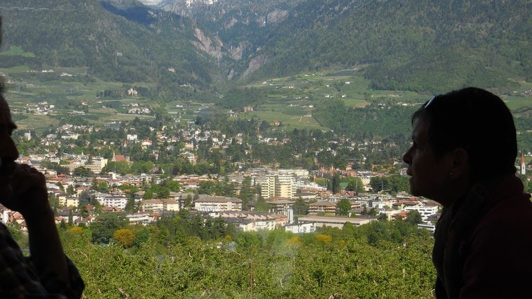 Bei der Fahrt mit der Vinschgaubahn eröffnet sich ein Weitblick auf Meran. Vor der Einfahrt im Bahnhof führt die Trasse oberhalb der traditionsreichen Kurstadt entlang.