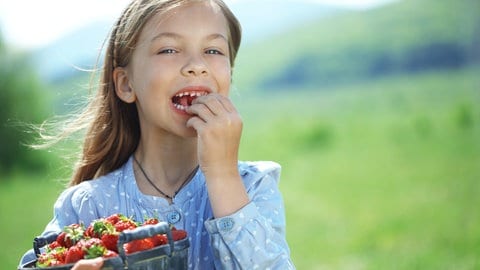 Ein Mädchen steht auf der Wiese, einen Eimer mit Erdbeeren im Arm