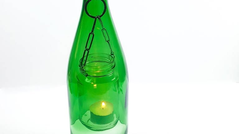 Ein Teelicht ins Glas stellen und die Metallkette von unten durch die abgeschnittene Glasflasche nach oben ziehen. Das Marmeladenglas schwebt nun in der Flasche.