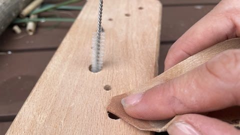 Nach dem Bohren die Späne vorsichtig aus dem Gang entfernen. Dies kann durch Klopfen oder auch mit dem feinen Bürstchen oder auch einem Staubsauger erfolgen. Die Eingänge aller Nistgänge mit etwas Schmirgelpapier glätten.