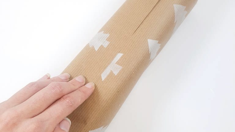 Ein Stück Geschenkpapier nehmen und die obere und untere Seite leicht überlappend über das zu verpackende Geschenk falten.