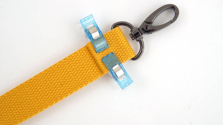 Ein Ende des Gurtbands um einen Taschenkarabiner legen, 1 cm nach innen einschlagen und mit Heftklammern fixieren.