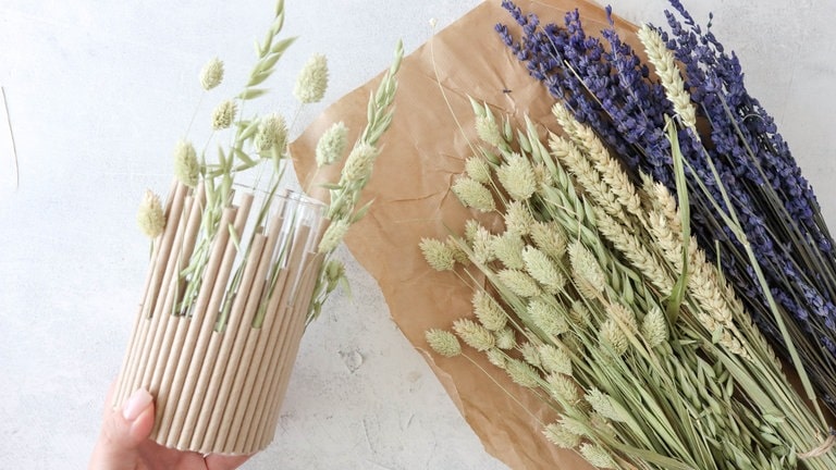 Die Trockenblumen nach Belieben um das Glas drumherum in die Strohhalme arrangieren, sodass sie gleichmäßig verteilt sind und einen schönen optischen Effekt erzeugen.