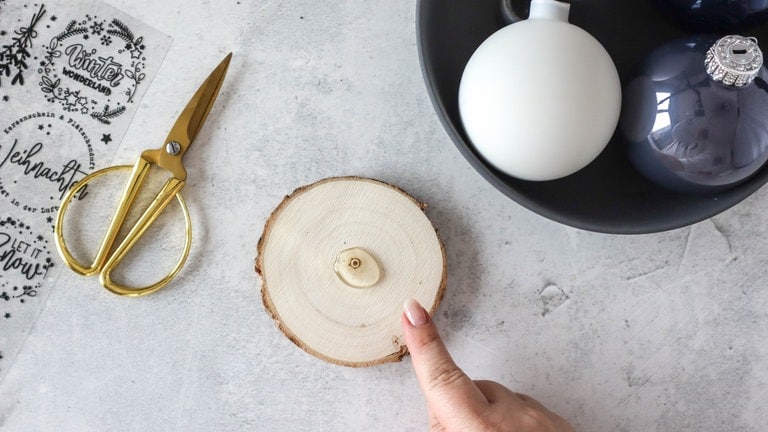 Um sicherzustellen, dass die Kugel stabil steht, wird sie mit Heißkleber oder Bastelkleber auf einer Holzscheibe befestigt.