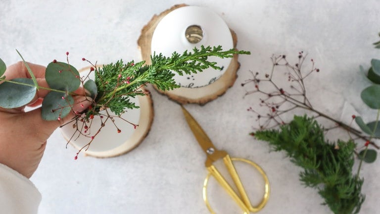 Die Kugel vorsichtig mit Wasser befüllen, damit die frische Greenery länger hält. Mit einer Blumenschere werden die weihnachtlichen Zweige und Pflanzen zurechtgeschnitten und in die Öffnung der Kugel gesetzt.