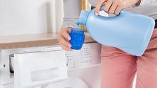 Eine Frau steht vor einer Waschmaschine und gießt Waschmittel in einen Behälter.