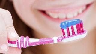 Eine junge frau hält eine Zahnbürste mit Zahnpasta drauf.