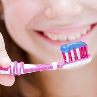 Eine junge frau hält eine Zahnbürste mit Zahnpasta drauf.
