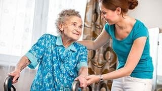 Eine junge Pflegekraft unterstützt eine alte Frau in deren Wohnung.