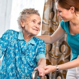 Eine junge Pflegekraft unterstützt eine alte Frau in deren Wohnung.