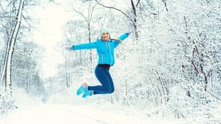 Frau springt in Schneelandschaft in die Luft