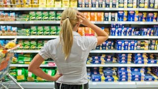 Frau steht ratlos vor Supermarktregal
