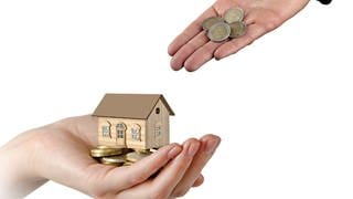 Hand mit Haus-Modell und Geld