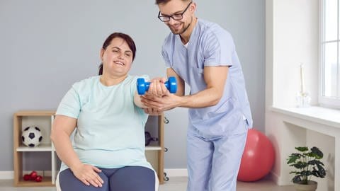 Frau trainiert mit Hantel unterstützt vom Physiotherapeuten
