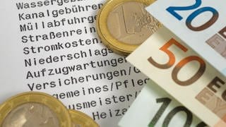 Geldscheine und Euro-Stück auf Liste mit Nebenkostenabrechnung
