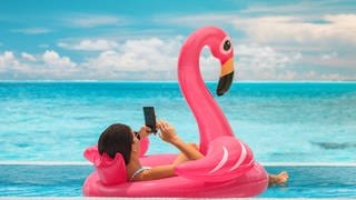 Frau am Smartphone in Flamingo-Boot - Telefonieren im Ausland