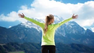 Frau steht mit ausgebreiteten Armen vor einer Bergkulisse - Einfaches Training für Brustwirbelsäule