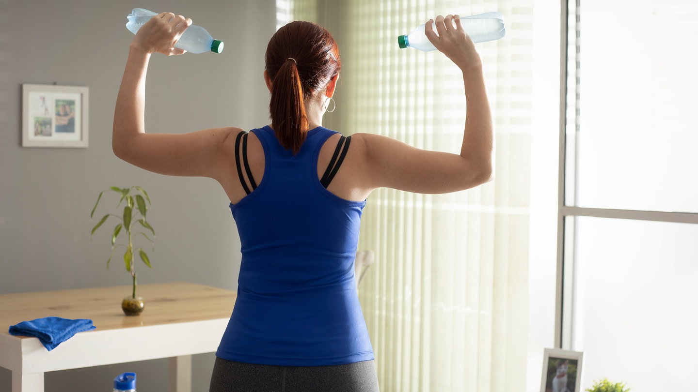 Fünf-Minuten-Fitness: Frau trainiert Schulter mit Wasserflaschen