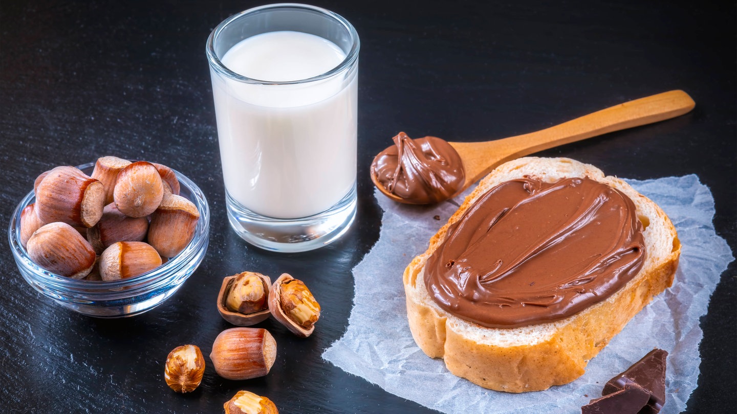 Schokocreme auf dem Brot mit einem Glas Milch und Haselnüssen