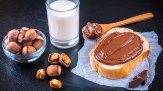 Schokocreme auf dem Brot mit einem Glas Milch und Haselnüssen